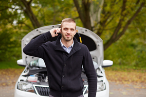 Man on cell phone in front of broken down car